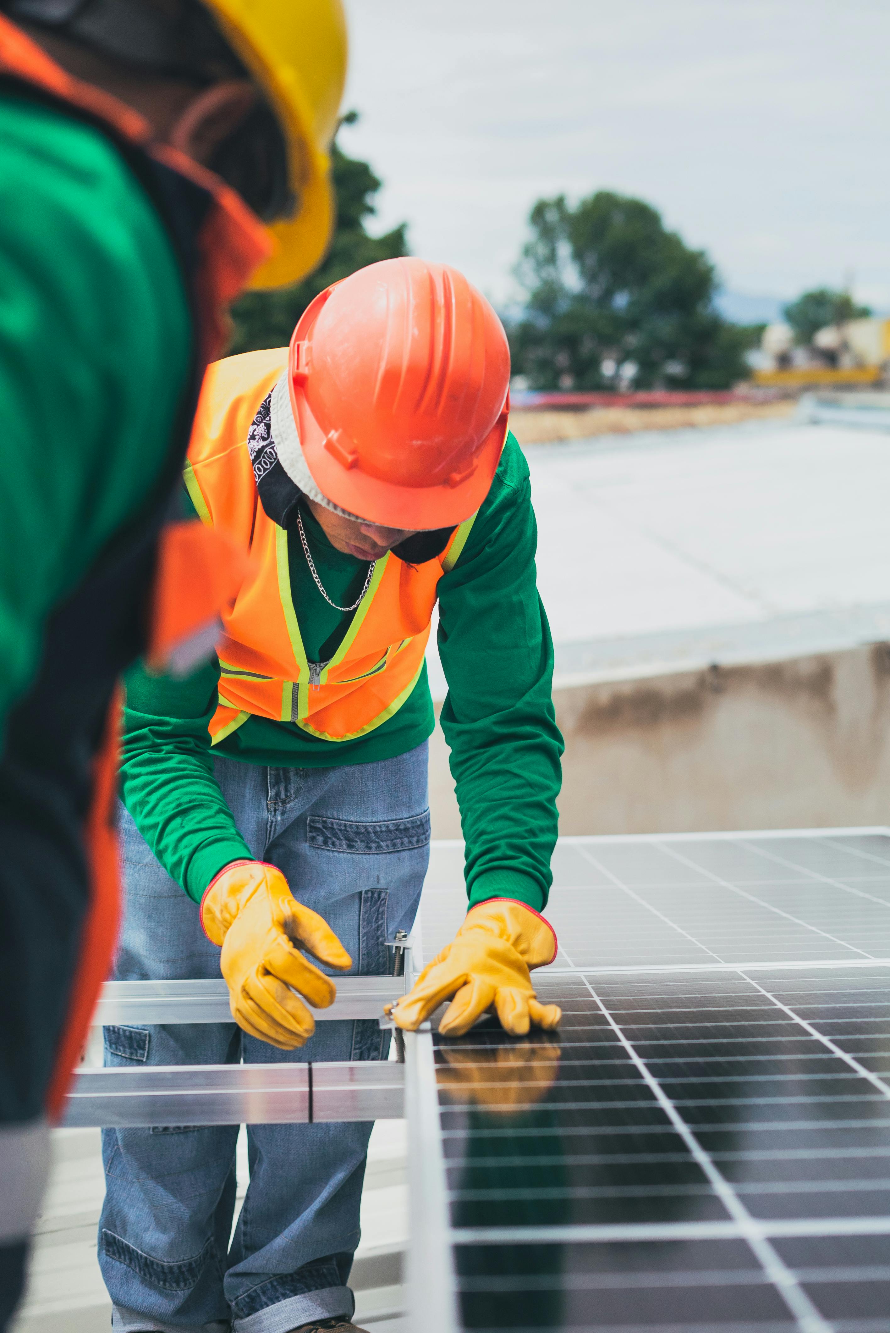 Worker in safety gear installing solar panels on a rooftop.